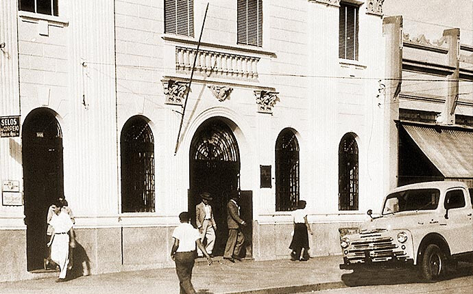 Bradesco: a história do maior banco privado do Brasil 2 Interior da agência original do Bradesco em Marília (SP) nos anos 1940, com balcões de madeira e funcionários em traje formal — a primeira sede do banco fundado por Amador Aguiar