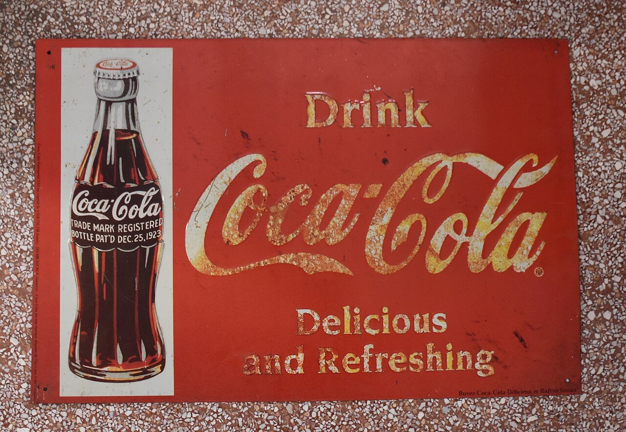 Placa esmaltada vintage de publicidade da Coca-Cola, estilo dos anos 1920, com o logotipo em caligrafia Spencerian e o slogan Delicious and Refreshing