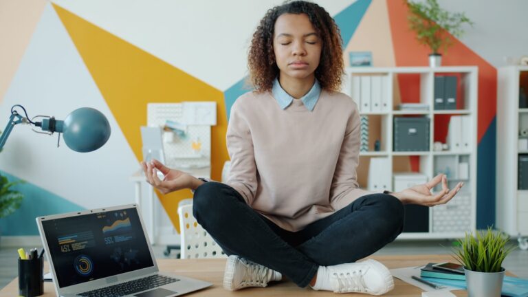 Profissional meditando em mesa de trabalho, representando bem-estar corporativo e saúde mental no ambiente profissional