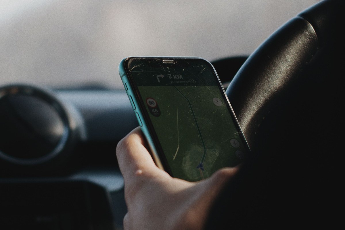 Mão segurando smartphone com aplicativo de navegação dentro de um carro, ilustrando o uso de apps de transporte no dia a dia