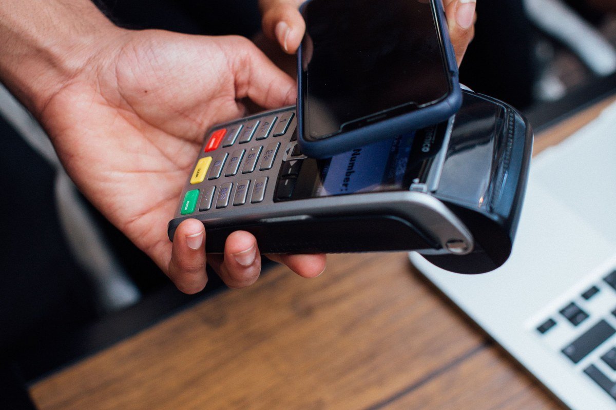 Mãos realizando pagamento por aproximação com smartphone em maquininha, ilustrando a expansão da 99 para serviços financeiros com a 99Pay