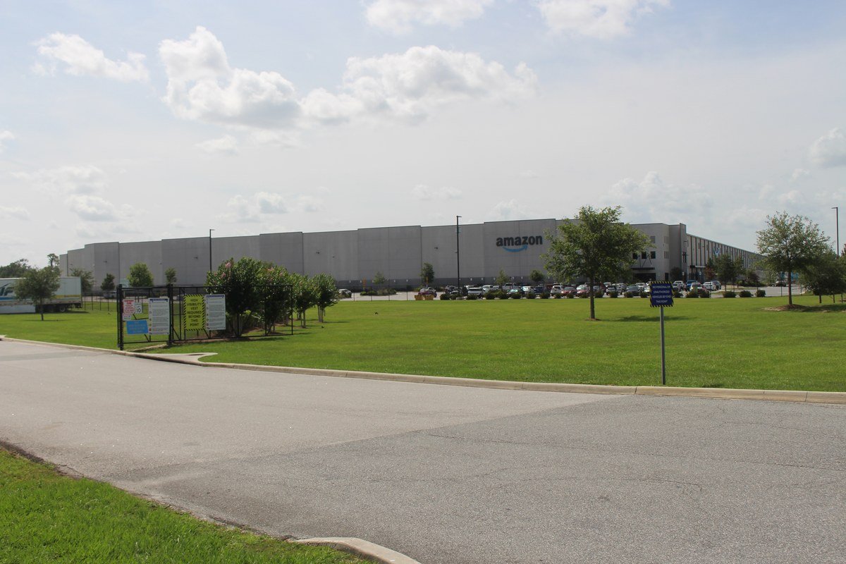 Fachada de um centro de distribuição da Amazon, com o logotipo da empresa visível, ilustrando a infraestrutura logística que sustenta o Prime