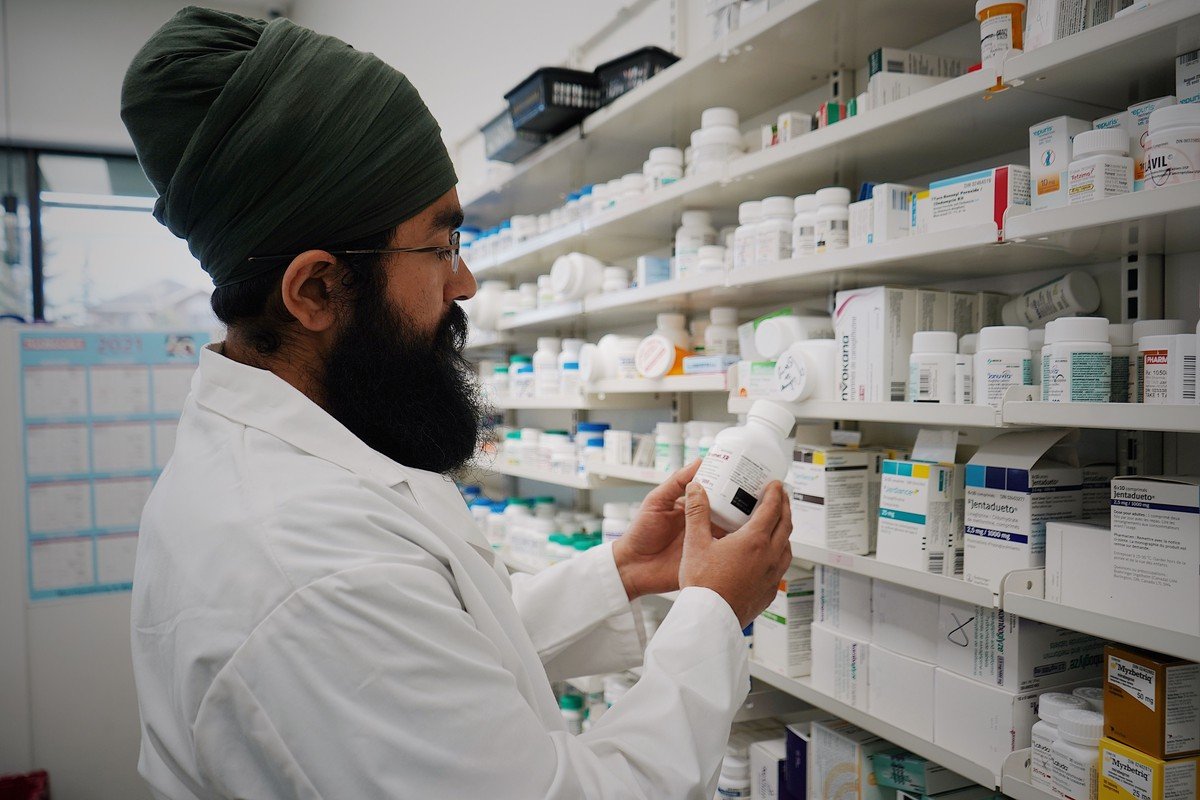 O atendimento farmacêutico no dia a dia da maior rede do país Farmacêutico verificando medicamento em prateleira de farmácia, ilustrando o atendimento cotidiano em redes como a Raia Drogasil