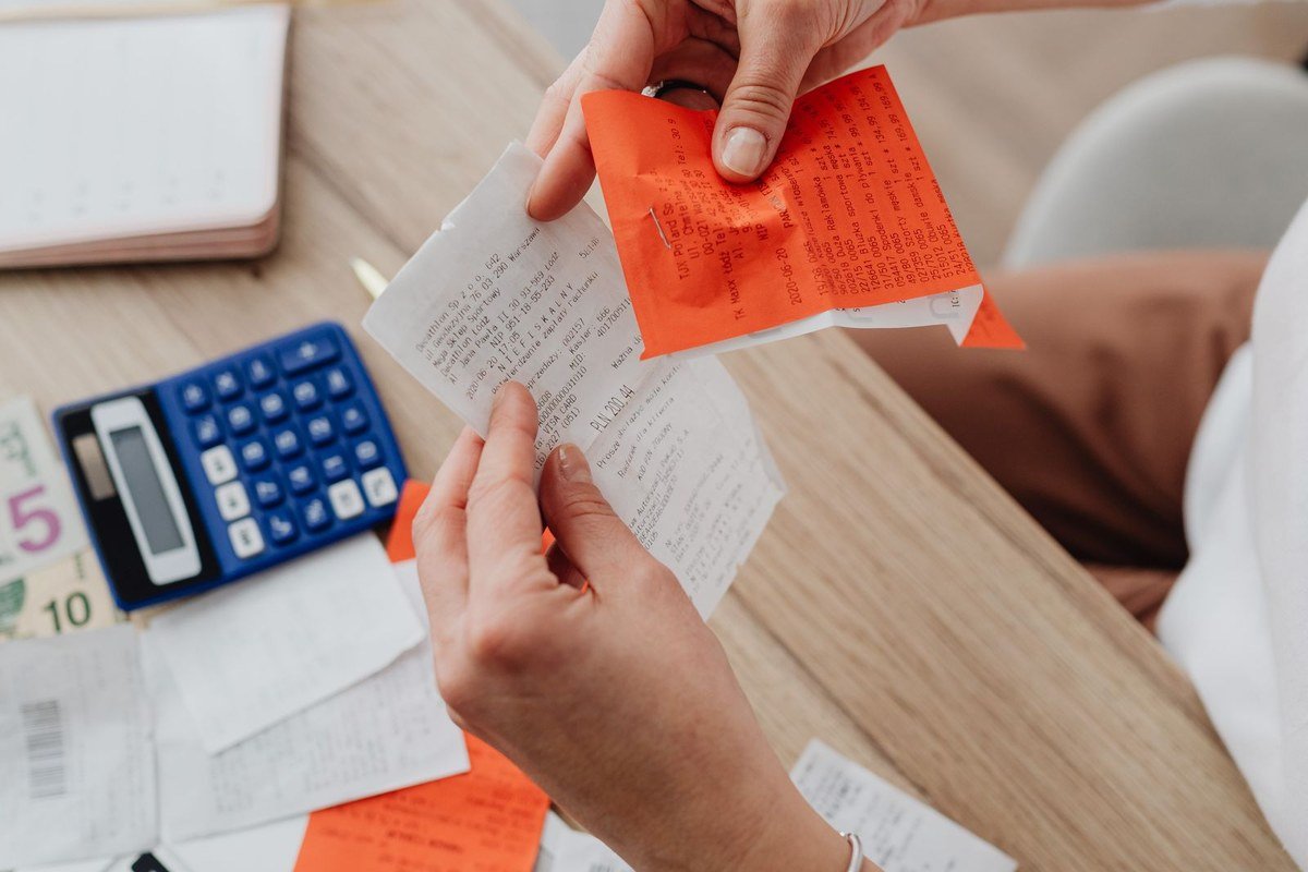 Calcular a própria inflação pessoal exige comparar os mesmos itens ao longo do tempo Pessoa conferindo recibos e notas de compras com calculadora sobre a mesa, ilustrando o cálculo da inflação pessoal