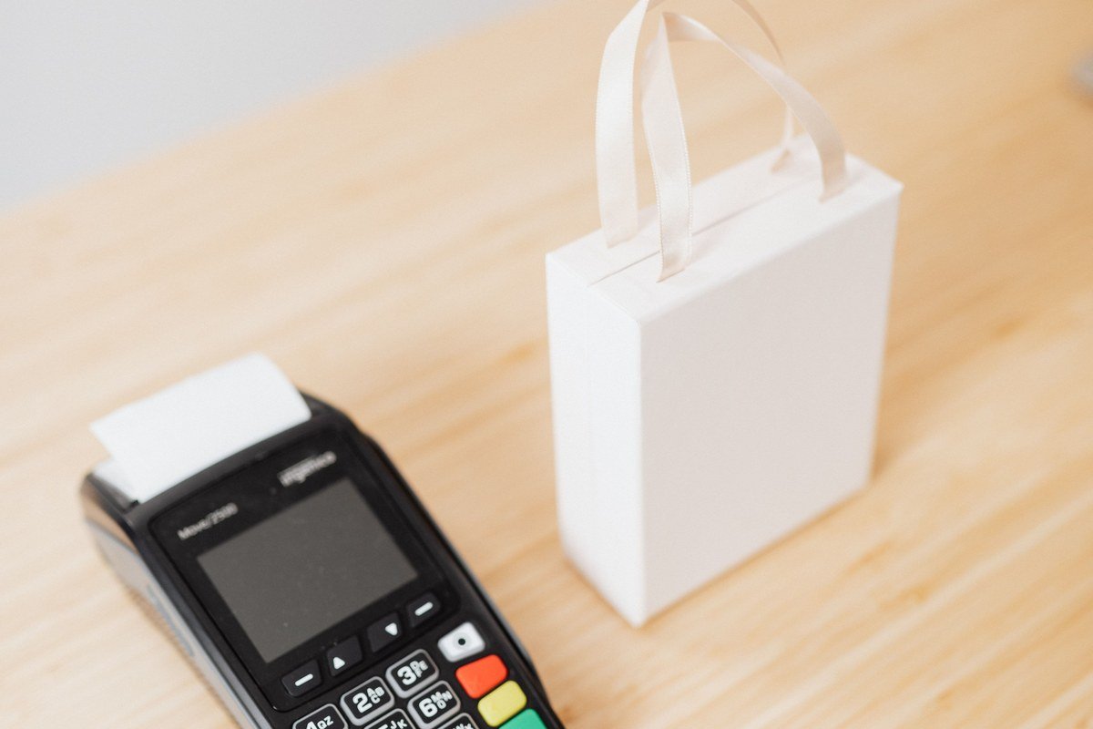 Maquininha de cartão sobre balcão de madeira ao lado de sacola de compras, ilustrando a popularização da maquininha da PagSeguro entre pequenos comerciantes