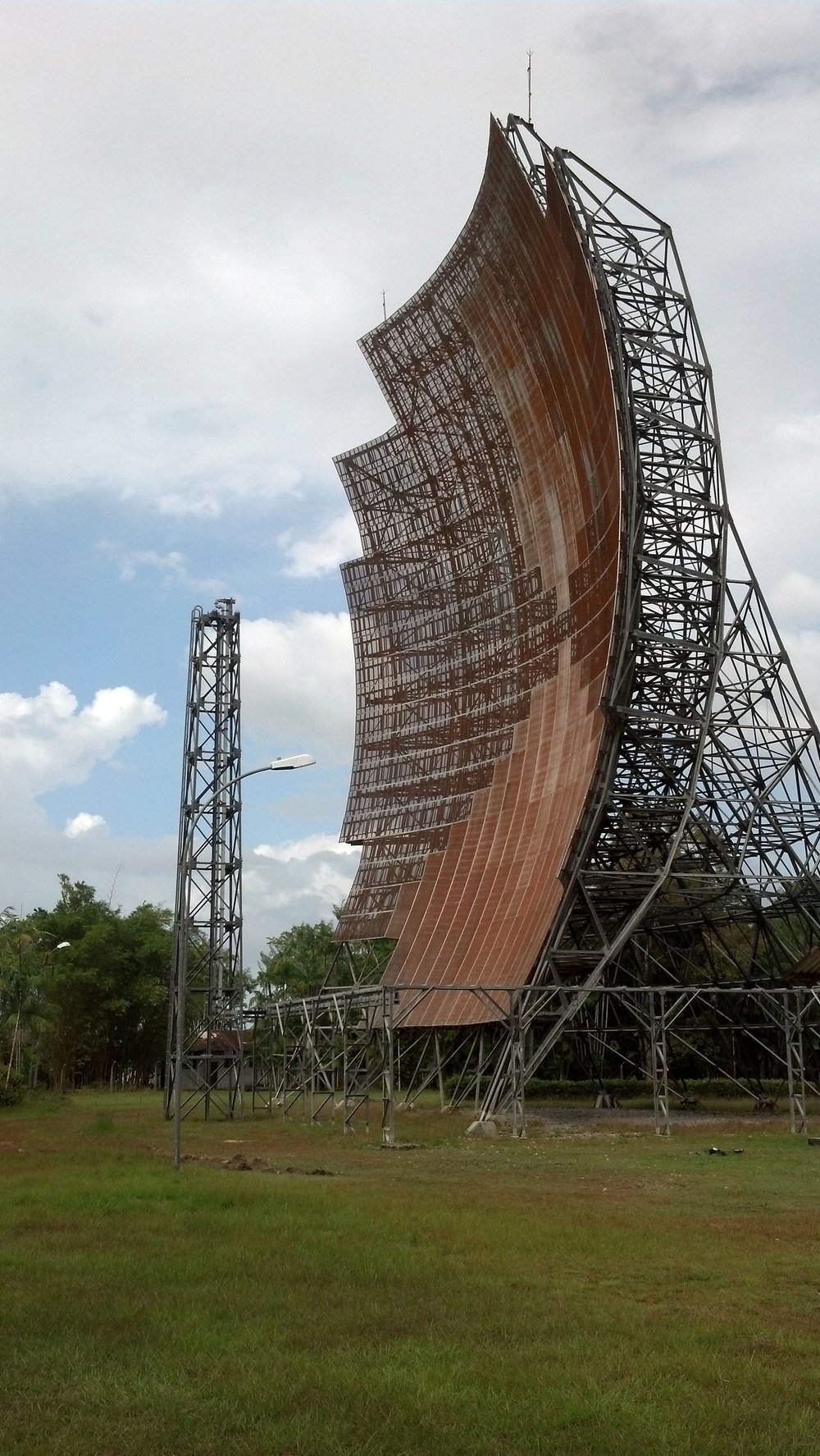 A Claro é brasileira? Quem é o dono da operadora, controlada pela mexicana América Móvil 5 Grande antena curva de rádio da Embratel, sustentada por uma estrutura metálica, em um terreno gramado sob céu nublado