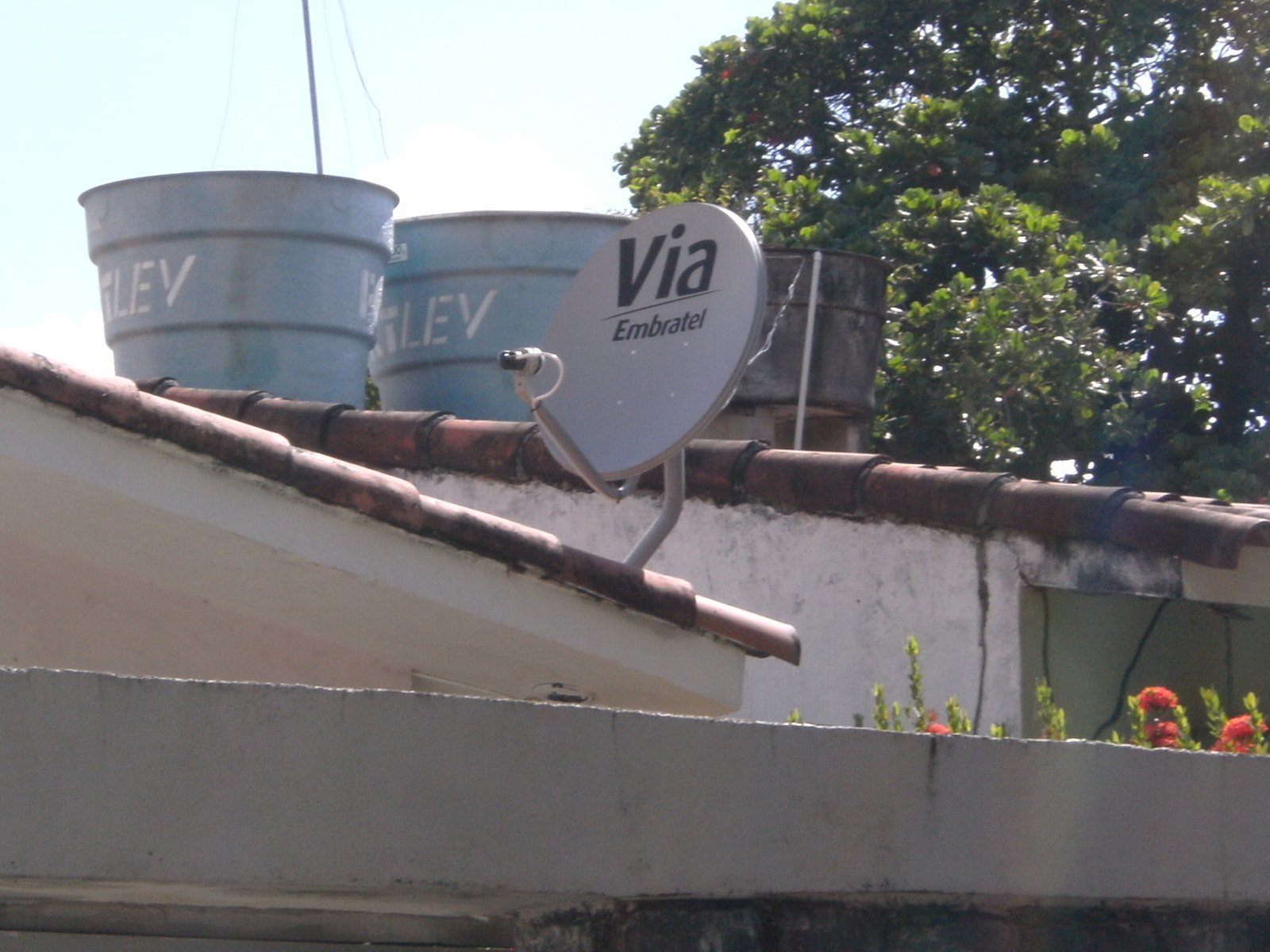 A Claro é brasileira? Quem é o dono da operadora, controlada pela mexicana América Móvil 6 Antena parabólica pequena com a marca Via Embratel instalada no telhado de uma casa, ao lado de caixas-d'água