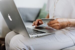 Pessoa segurando cartão ao usar um computador, ilustrando o pagamento de uma fatura
