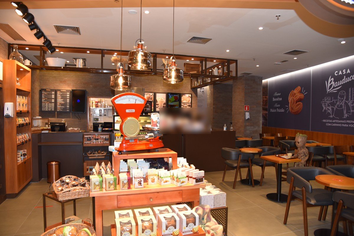 Interior de uma loja Casa Bauducco, com balança antiga, caixas de panetone e mesas de café
