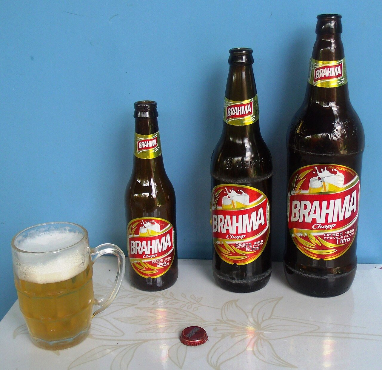 Três garrafas de cerveja Brahma de tamanhos diferentes e uma caneca de chope sobre uma mesa