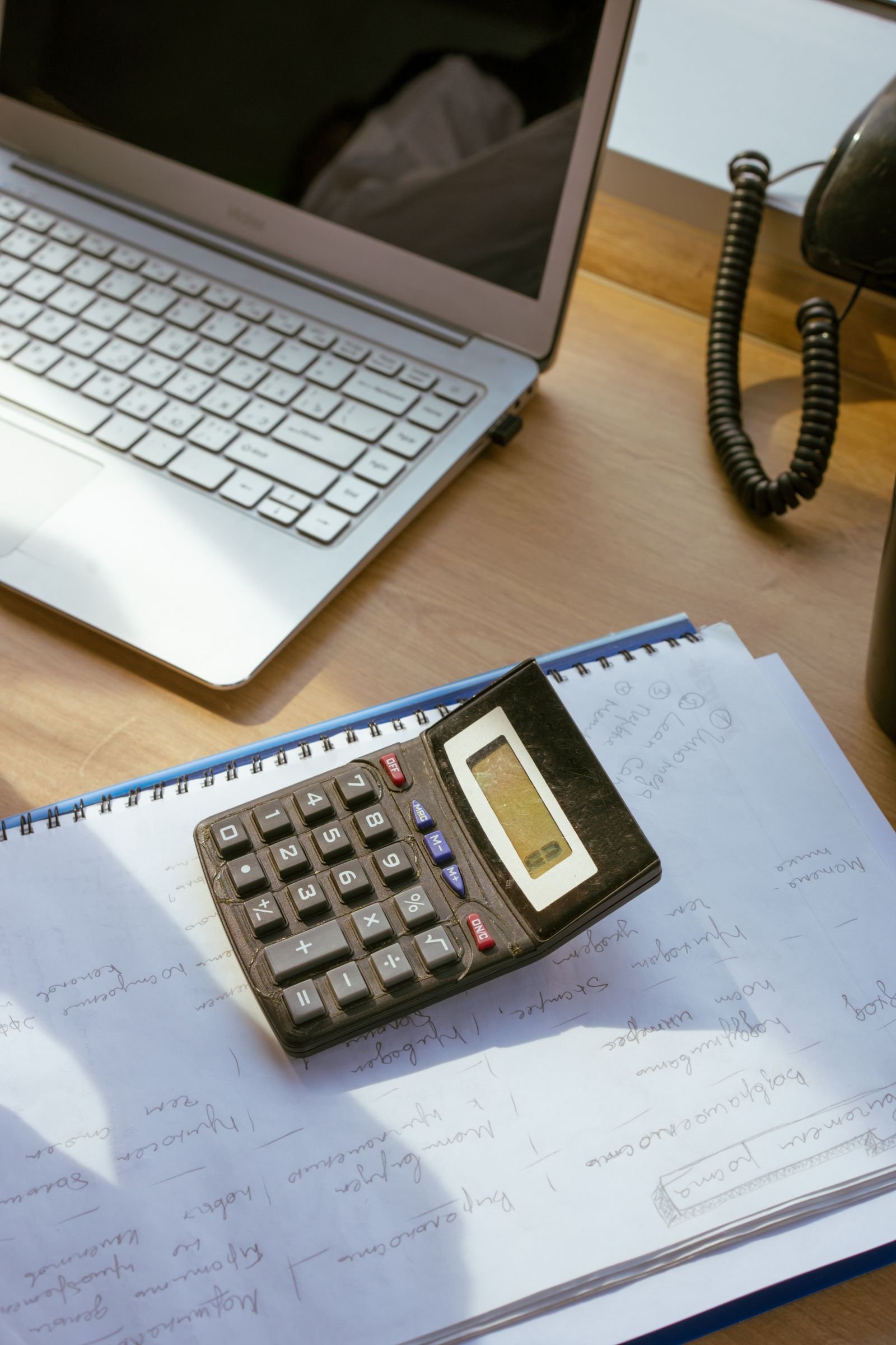 Calculadora sobre caderno e documentos ao lado de um computador, ilustrando a conferência de uma proposta de crédito.
