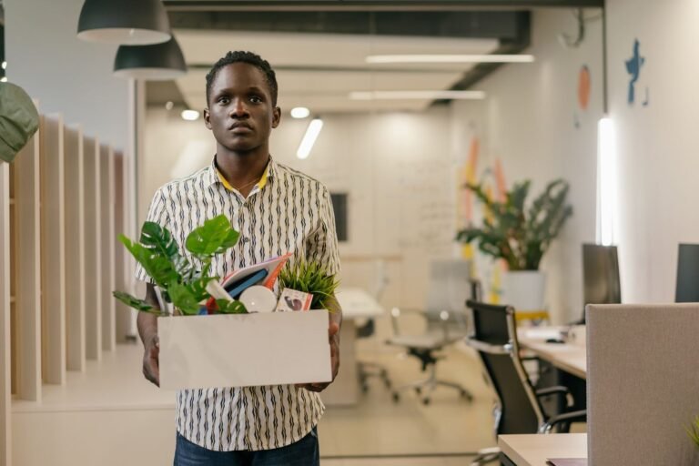 Homem segurando uma caixa com plantas e objetos pessoais em um escritório