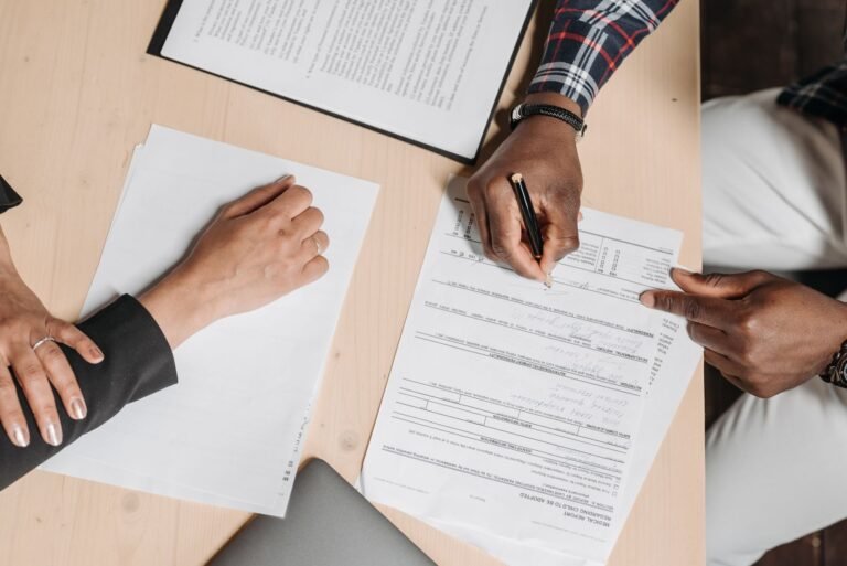 Pessoas conferindo documentos sobre uma mesa, em foto ilustrativa