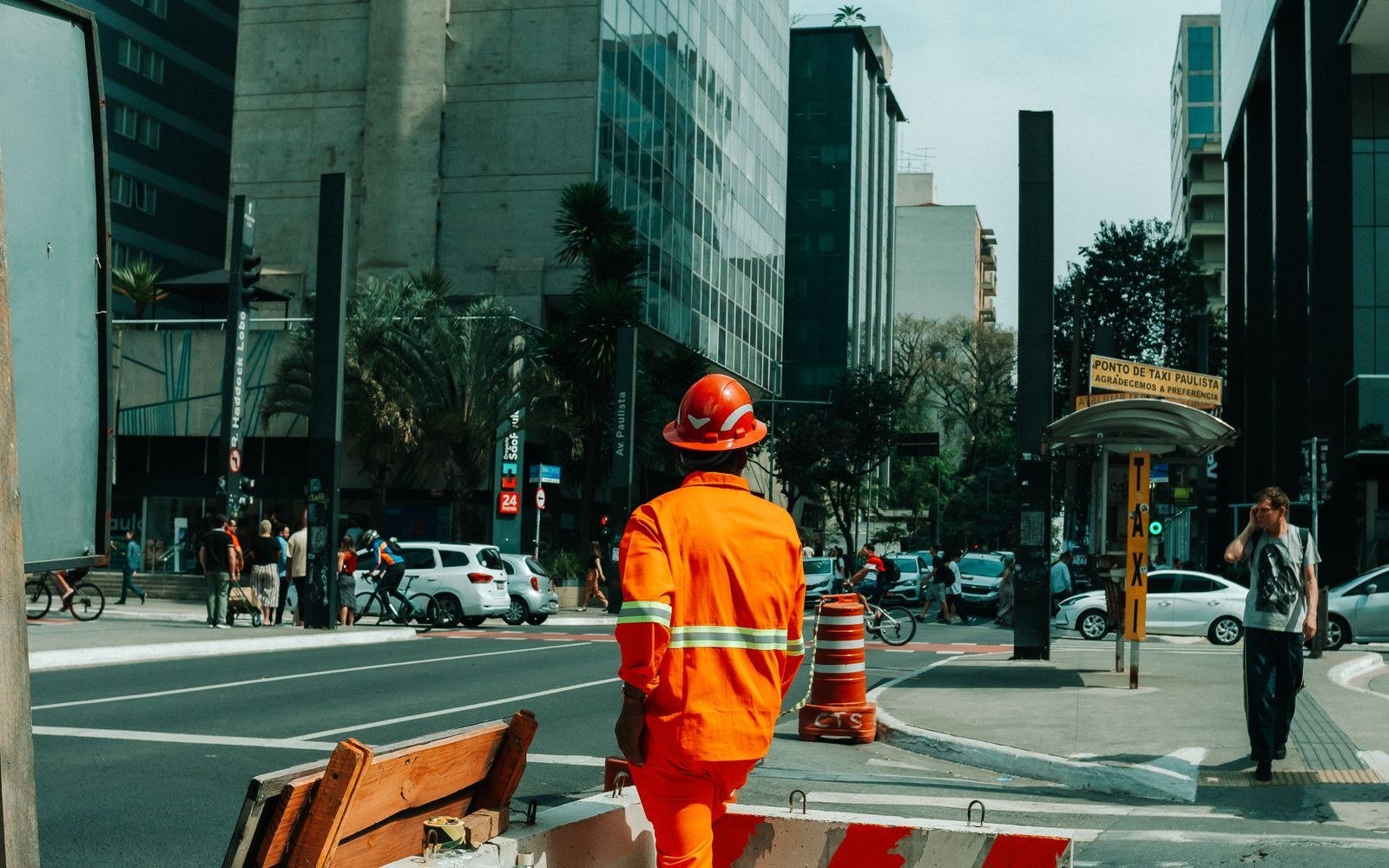 Demissão sem justa causa: direitos, aviso prévio, multa do FGTS e cálculo 3 Trabalhador de uniforme laranja e capacete atravessando uma avenida em São Paulo