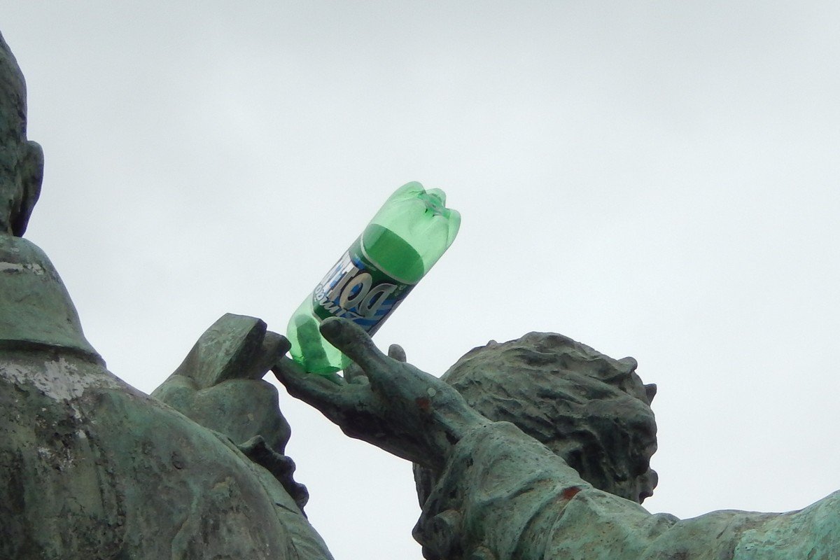 Garrafa verde de refrigerante Dolly sabor limão apoiada na mão de uma estátua de bronze, contra o céu nublado