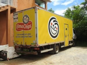 Caminhão amarelo com o nome e o rosto sorridente da Elma Chips em São José do Almeida, Minas Gerais, em 2024