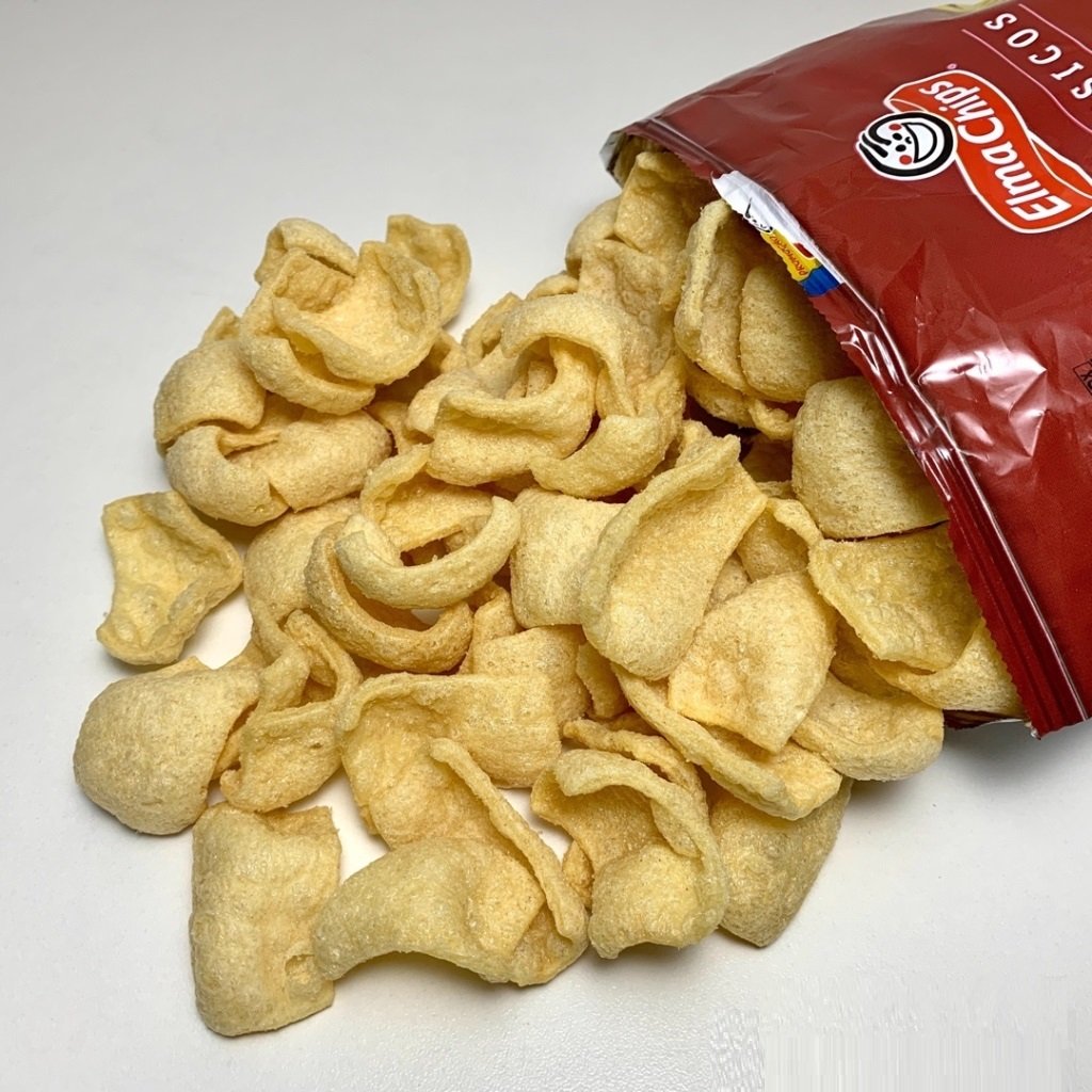 Salgadinhos ao lado de uma embalagem vermelha com o nome e o rosto sorridente da Elma Chips