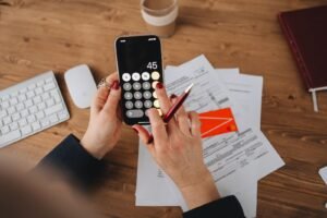 Pessoa usando a calculadora do celular sobre documentos financeiros para conferir valores.