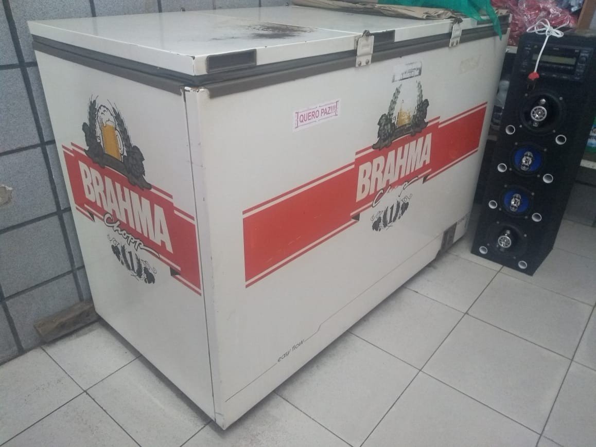 Freezer horizontal branco com a marca Brahma pintada em vermelho, ao lado de uma caixa de som