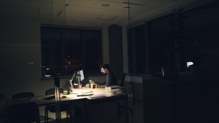 Profissional trabalhando sozinho à noite em um escritório escuro, iluminado pela luz da mesa