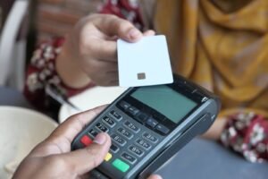 Mão aproximando um cartão de crédito de uma maquininha para pagar