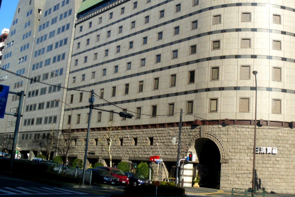 Prédio de pedra e concreto com fachada curva e a placa da Nissin em japonês, na sede da empresa em Tóquio