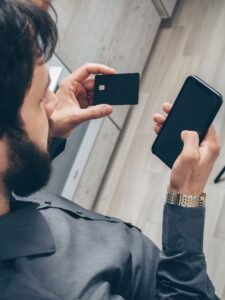 Pessoa segurando celular e cartão, em foto ilustrativa de serviços financeiros