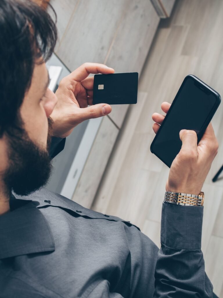Pessoa segurando celular e cartão, em foto ilustrativa de serviços financeiros