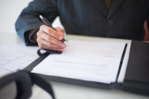 Mão segurando caneta sobre documentos, ilustrando a análise de um contrato de crédito