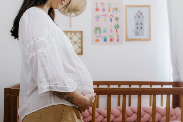 Gestante ao lado de um berço em quarto de bebê; foto ilustrativa