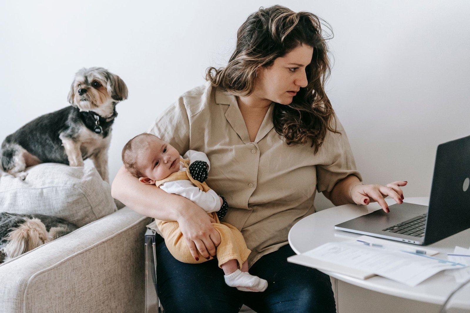 Salário-maternidade: quem tem direito, inclusive desempregadas e MEIs 3 Mãe com o bebê no colo trabalhando no notebook em casa. Foto ilustrativa para a seção sobre MEI e autônomas.