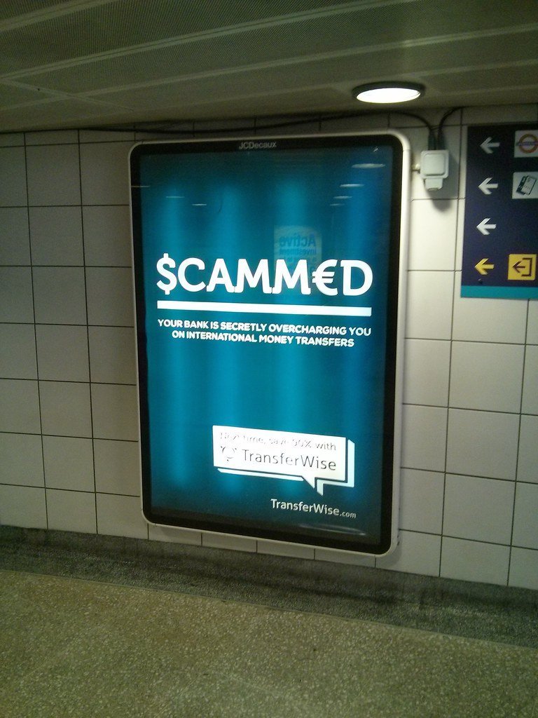 Painel iluminado no metrô de Londres com o anúncio Scammed, da TransferWise, que diz que os bancos cobram taxas escondidas em transferências internacionais