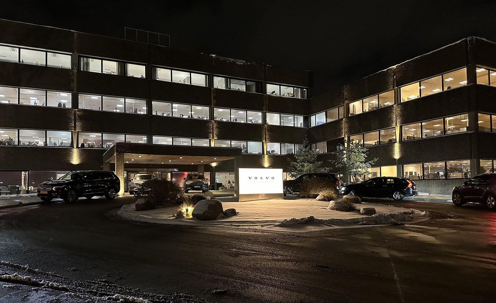 Prédio de escritórios da sede da Volvo Cars em Gotemburgo, iluminado à noite, com carros estacionados na entrada
