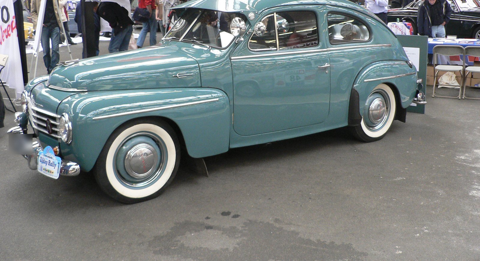 Volvo PV444 verde-azulado de 1951, com pneus de faixa branca, exposto em um salão de carros antigos